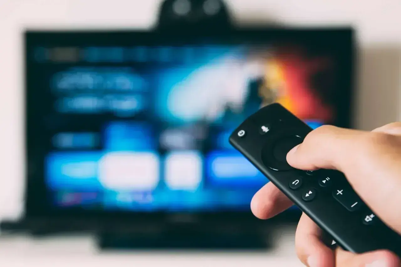 Dłoń trzymająca pilot do telewizora, ekran pokazuje menu. Dowiedz się, jak odbierać TV naziemną bez anteny, korzystając z nowoczesnych rozwiązań.