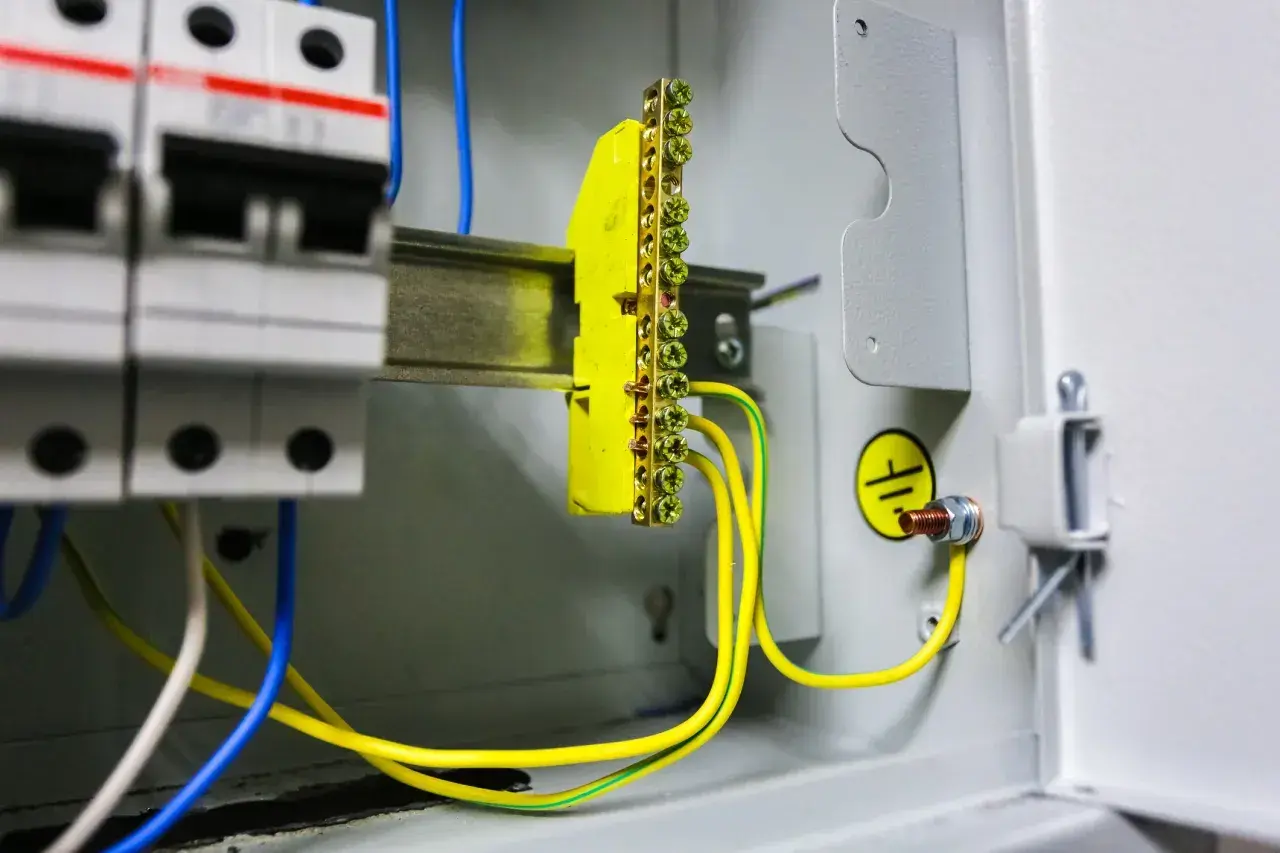 W skrzynce elektrycznej widać wyłączniki i żółto-zielone przewody tworzące uziemienie. Symbol uziemienia potwierdza bezpieczeństwo instalacji.