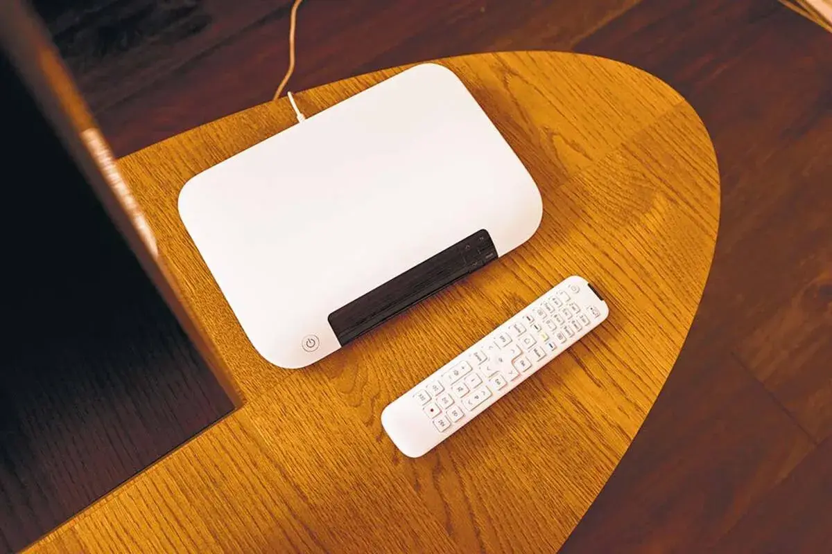Biały router i pilot leżą na drewnianym stoliku. Chcesz wiedzieć, jak zmienić hasło do internetu Orange?