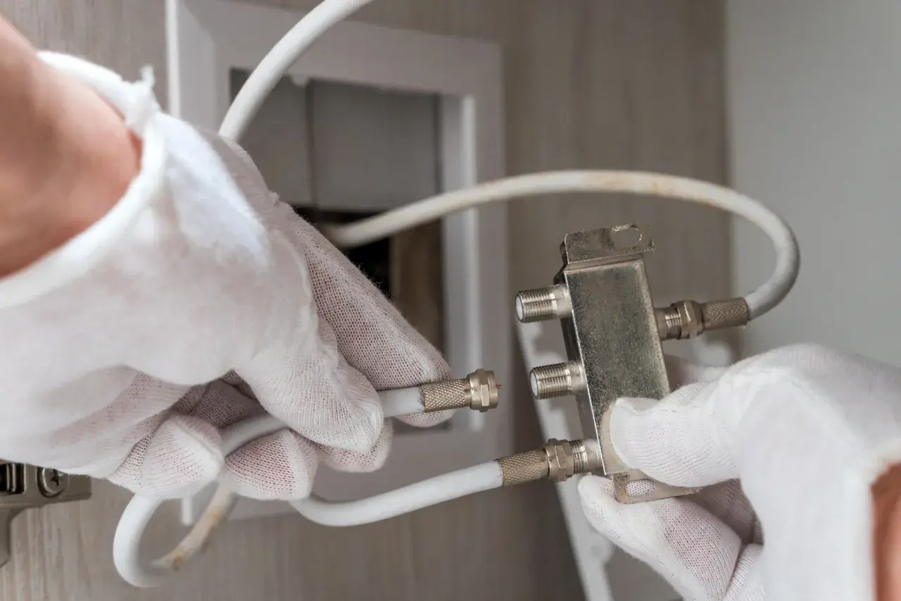 Ręce w białych rękawiczkach podłączają kabel antenowy do rozdzielacza.
