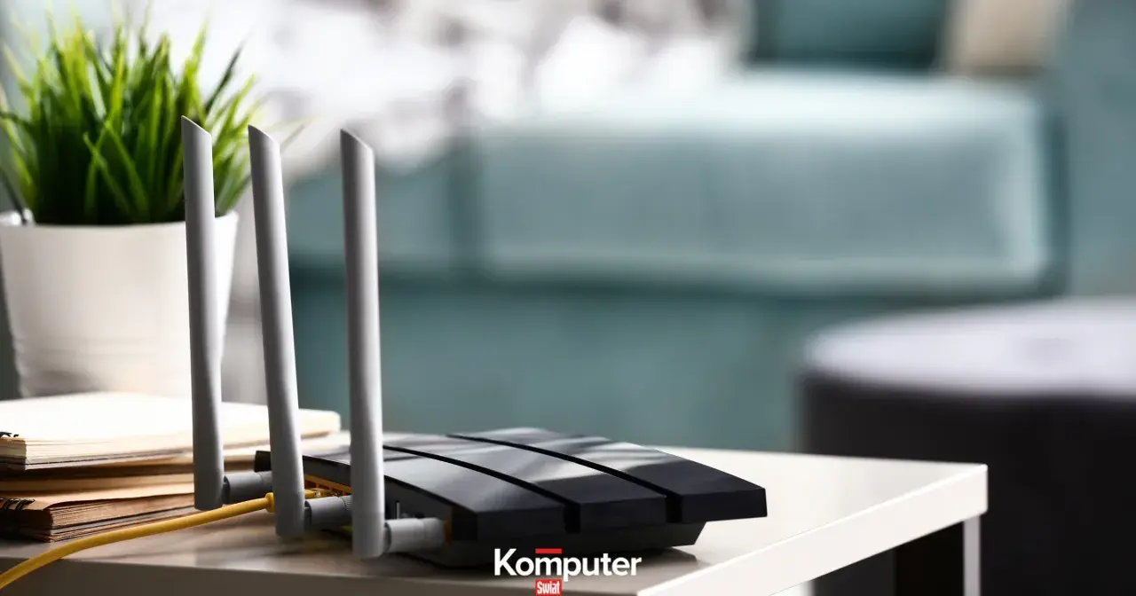 Jak podłączyć dysk do routera? Czarny router z antenkami i żółtym kablem na stoliku, obok doniczka z zieloną rośliną.