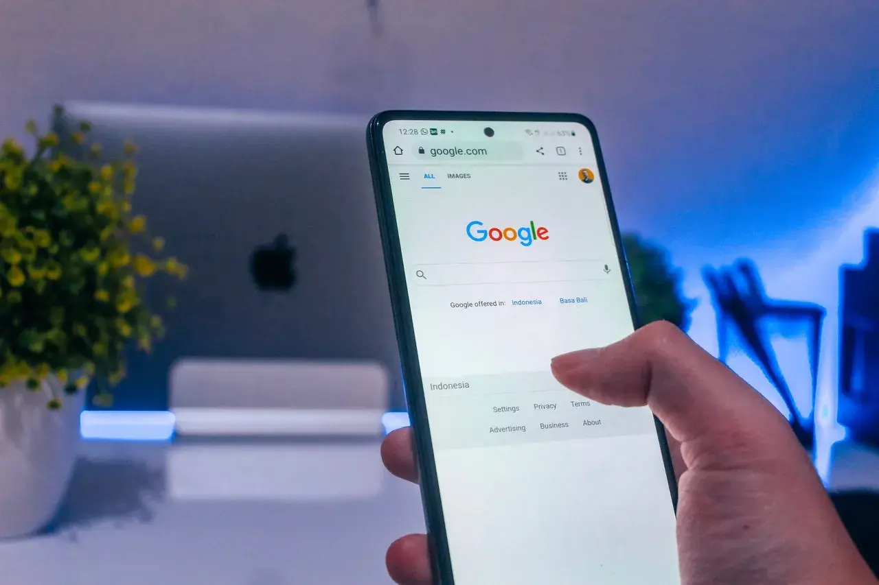 Palec dotyka ekranu telefonu z widoczną wyszukiwarką Google. Dowiedz się, jak wylogować się z konta Google, aby zwiększyć prywatność.