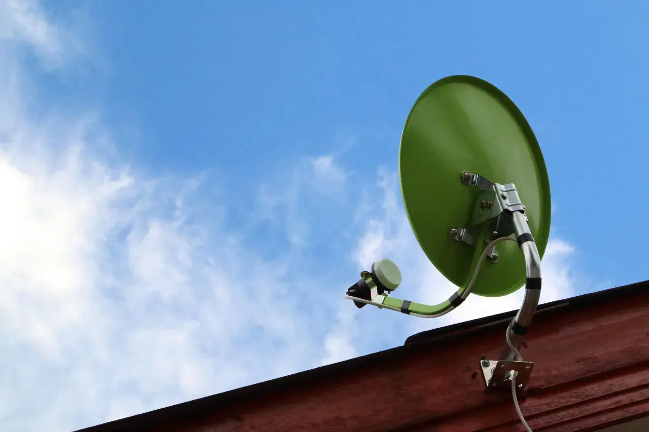 Zielona antena satelitarna zamontowana na drewnianej ścianie, gotowa do odbioru sygnału. Dowiedz się, jak zamontować antenę satelitarną.