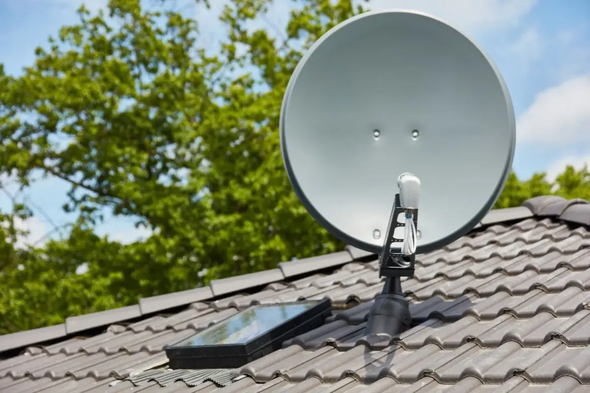 Antena satelitarna na dachu, obok okna dachowego. Prawidłowe ustawienie to klucz do tego, jak poprawić jakość sygnału satelitarnego.