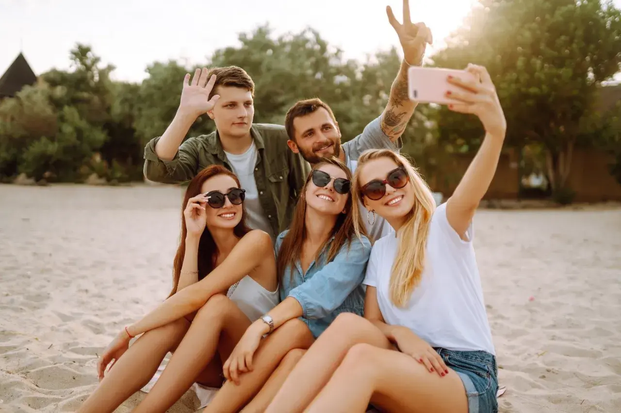 Grupa przyjaciół robi selfie na plaży. Zastanawiasz się, jak sprawdzić, czy roaming jest włączony Plus abonament? Sprawdź to przed wyjazdem!
