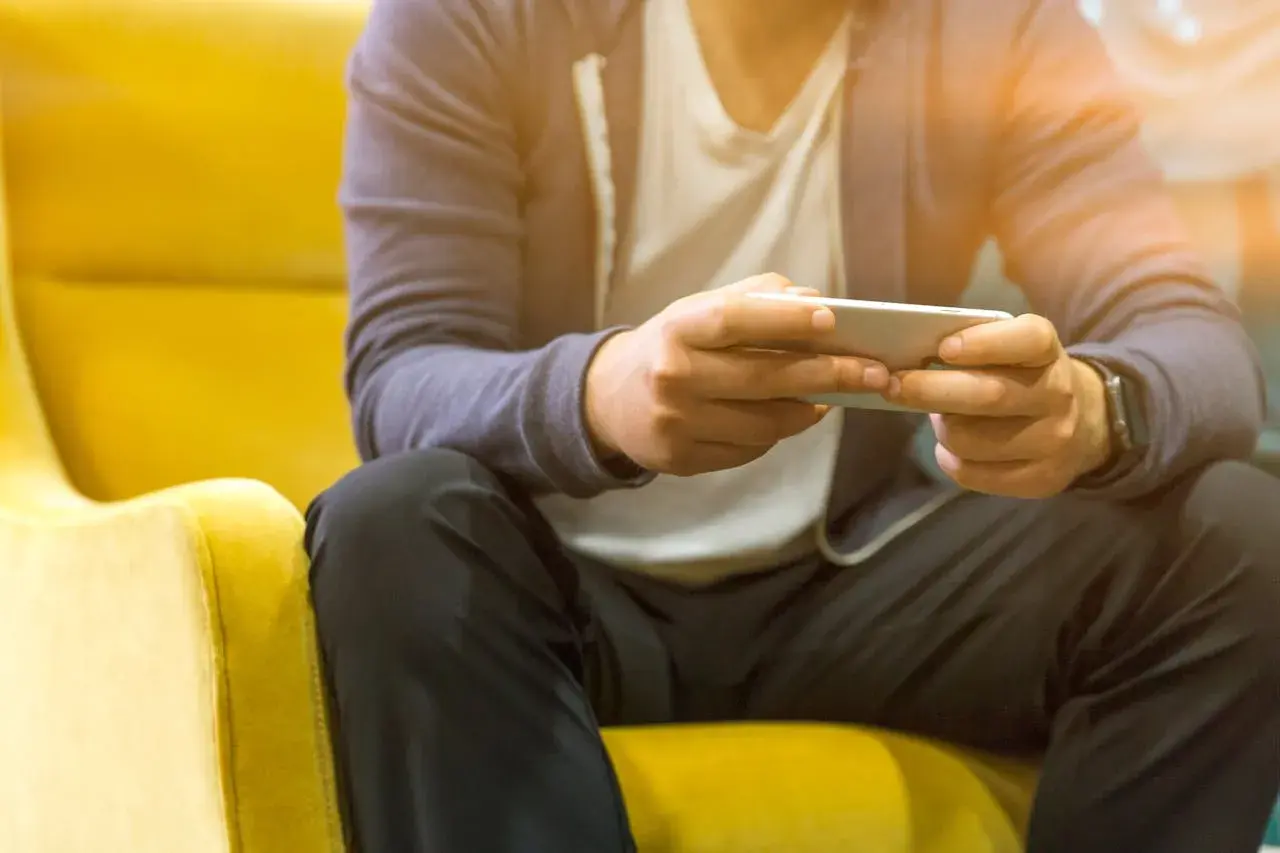 Mężczyzna siedzi na żółtym fotelu, trzymając telefon. Czy telefon bez karty SIM połączy się z Wi-Fi? Tak, to możliwe.