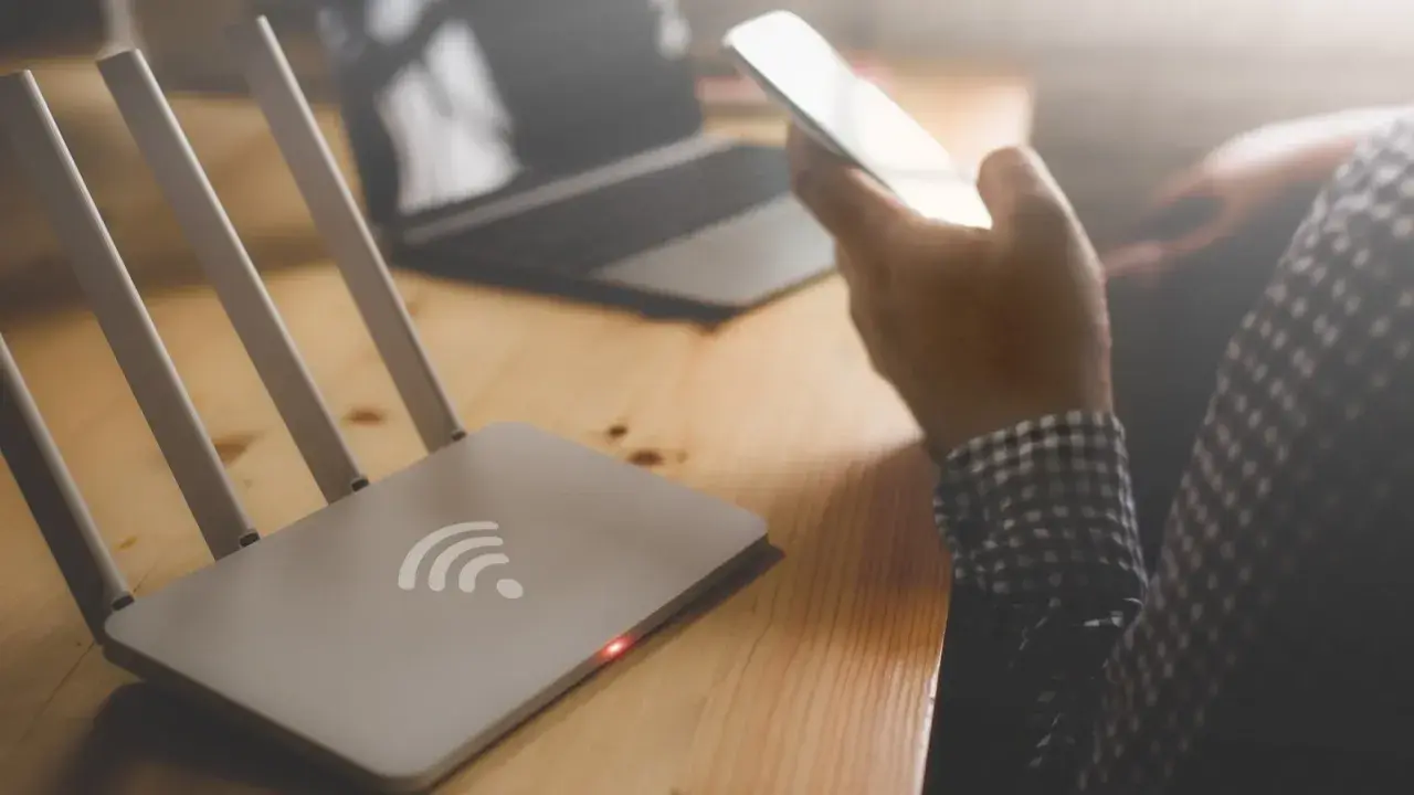 Router i osoba trzymająca telefon, zastanawiająca się, dlaczego wifi samo się wyłącza w telefonie.