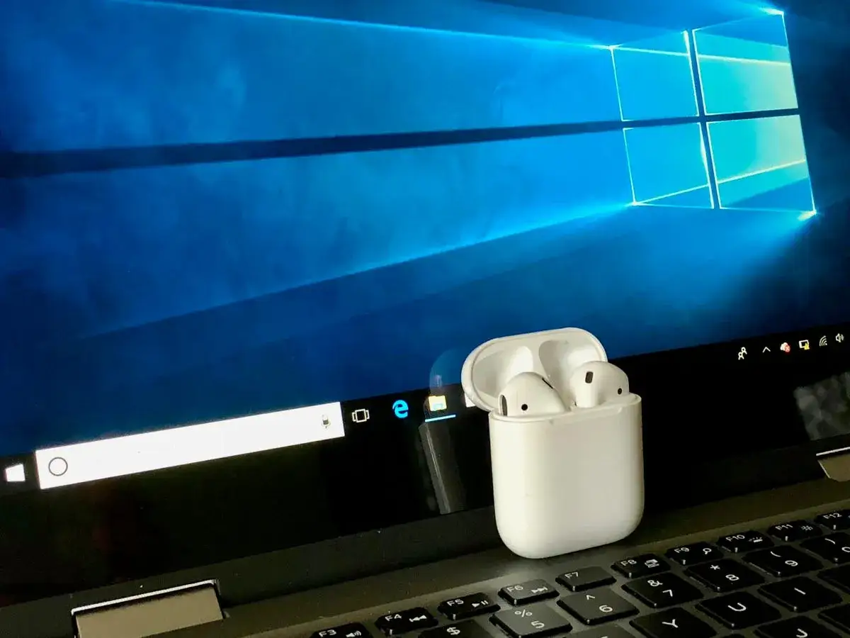AirPods w etui na klawiaturze laptopa z ekranem Windows. Prosty sposób, jak połączyć AirPods z laptopem.