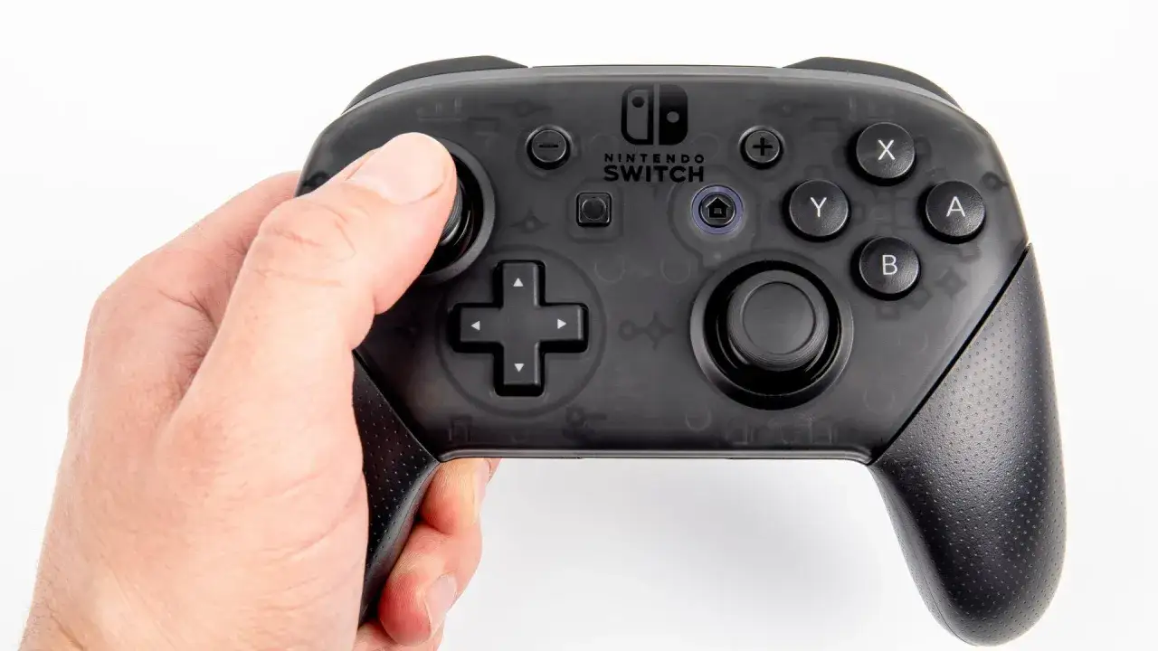 Dłoń trzyma czarny kontroler Nintendo Switch Pro. Dowiedz się, jak podłączyć pada Nintendo do PC, by cieszyć się grami na większym ekranie.