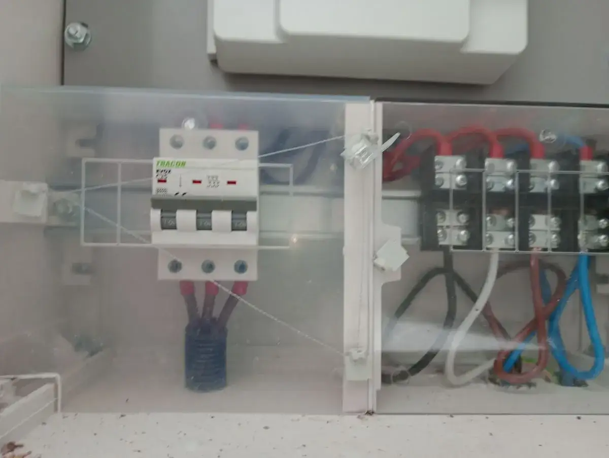 Zabezpieczenie przedlicznikowe w skrzynce elektrycznej. Trójfazowy wyłącznik i listwa zaciskowa z przewodami.