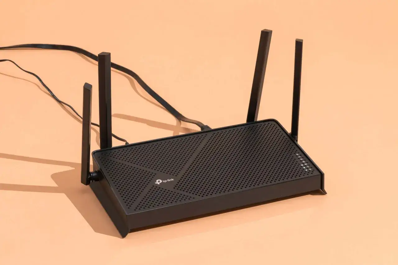 Czarny router TP-Link z antenkami, podłączony do zasilania. Dowiedz się, jak przyspieszyć internet w laptopie, optymalizując sygnał Wi-Fi.