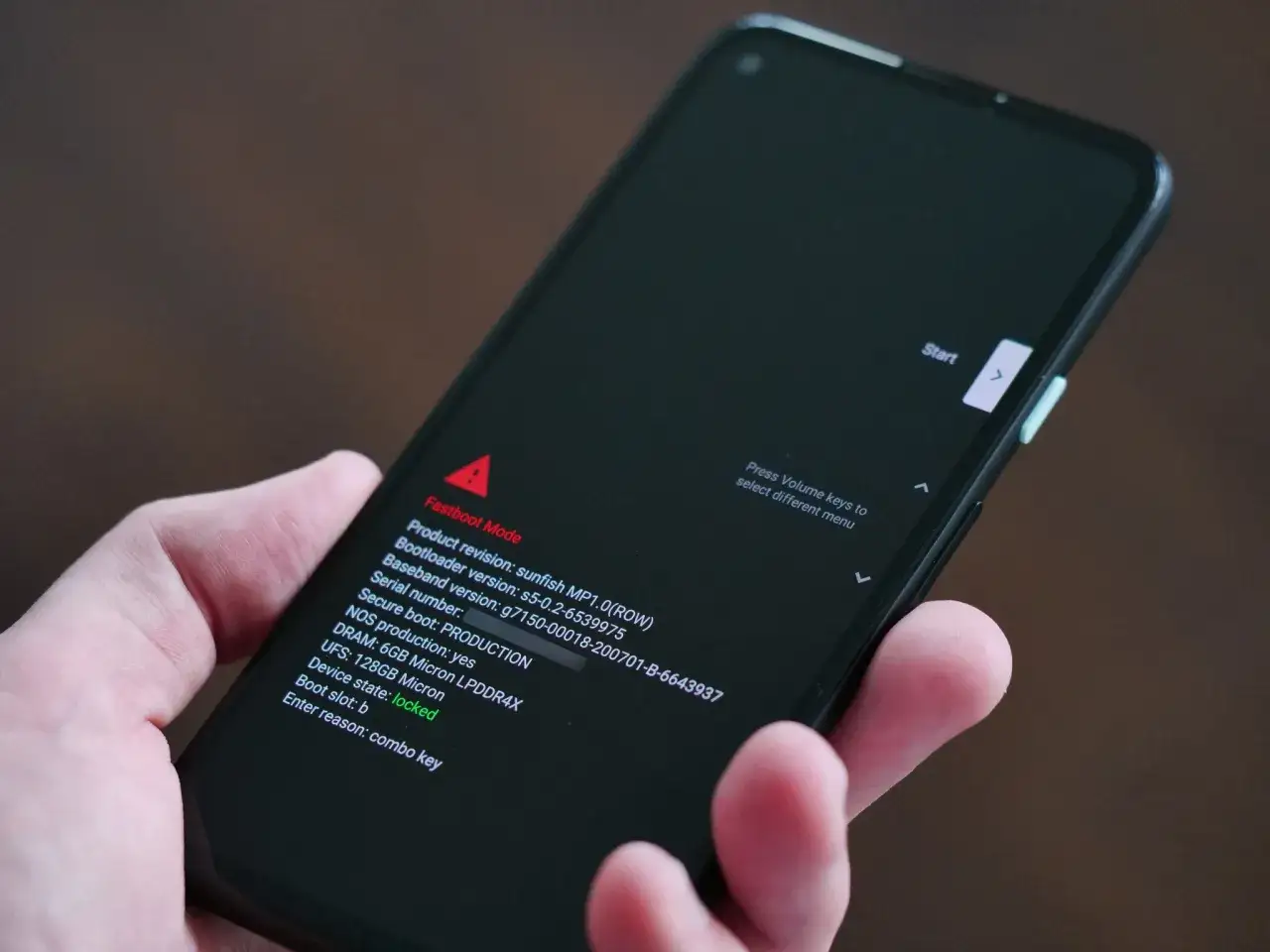 Dłoń trzyma smartfon z włączonym trybem fastboot. Na ekranie widoczne są informacje o wersji oprogramowania i stanie urządzenia.