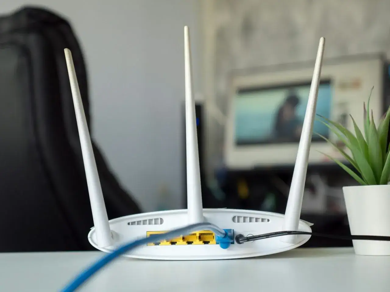 Router z trzema antenami, podłączony niebieskim kablem. Dowiedz się, jak podłączyć wzmacniacz wifi do routera, by wzmocnić sygnał.